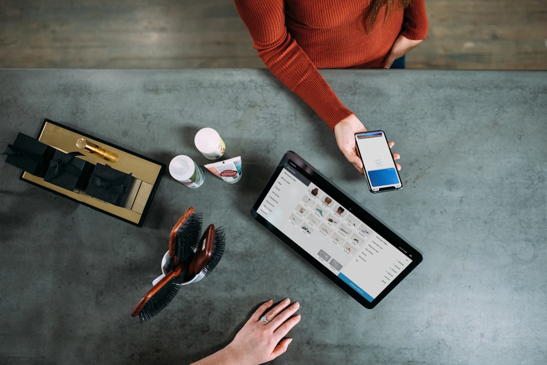 hero-gallery-03 Overhead view of business consultation featuring smartphone payment and tablet product display. Modern salon or retail workspace with coffee cups and professional tools showcases contemporary customer experience.